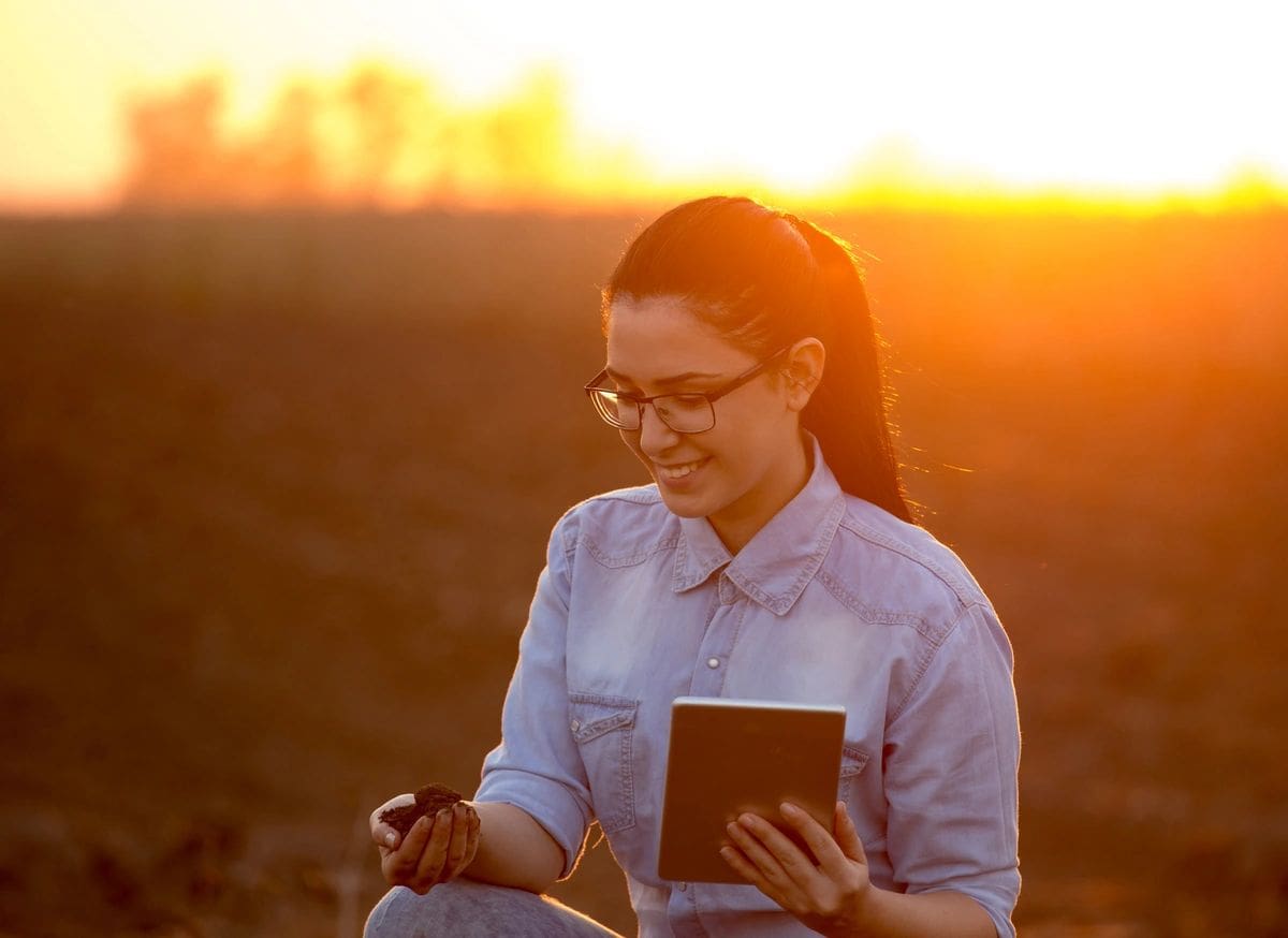 A woman in glasses is holding a book and looking at her phone.