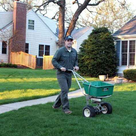 A man in grey shirt pulling green cart on grass.